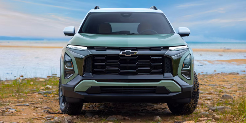 Green Chevrolet SUV parked on a rocky shoreline with a coastal landscape in the background.