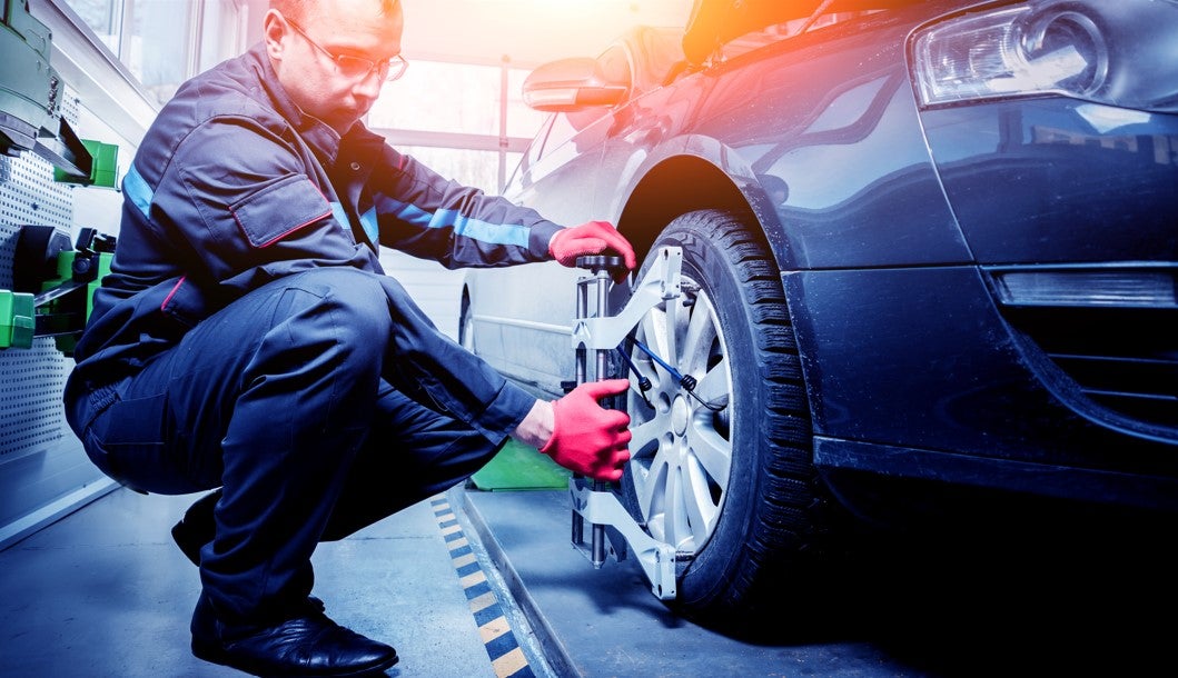 Automotive technician performing a wheel alignment service on a vehicle in a repair shop.