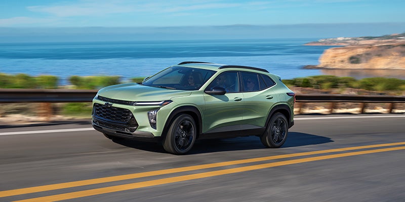 Green Chevrolet SUV driving along a coastal highway with ocean views in the background.